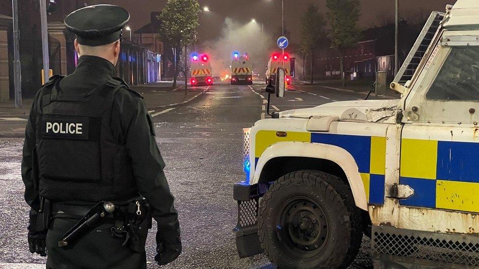 A PSNI officer stands beside a police Land Rover at the scene of rioting in Belfast