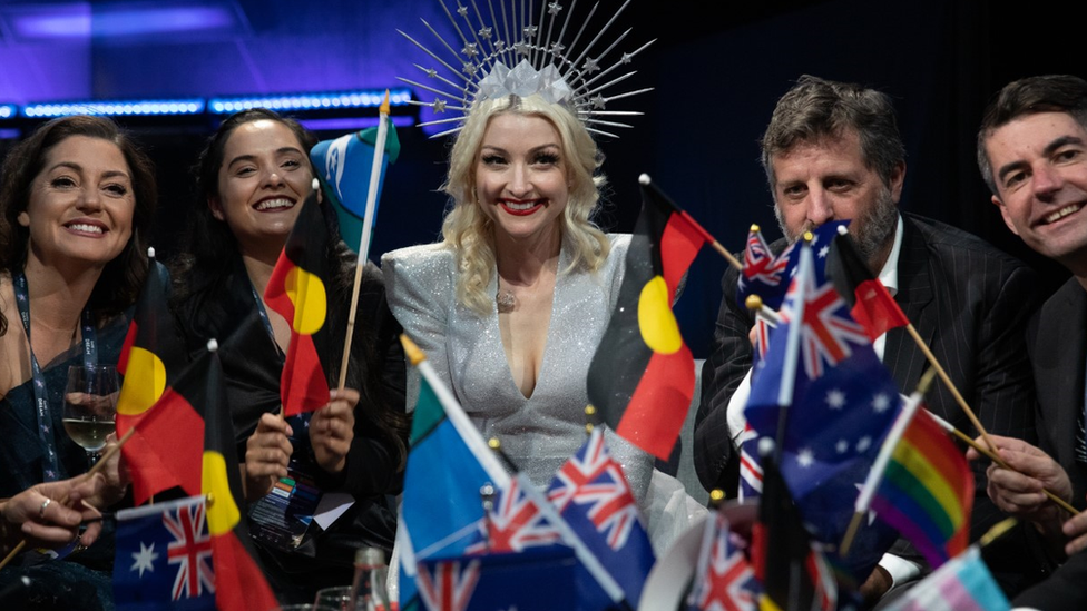 Australia's 2019 performer Kate Miller-Heidkes surrounded by her team waits for vote results while waiving Australian and Aboriginal flags in Tel Aviv