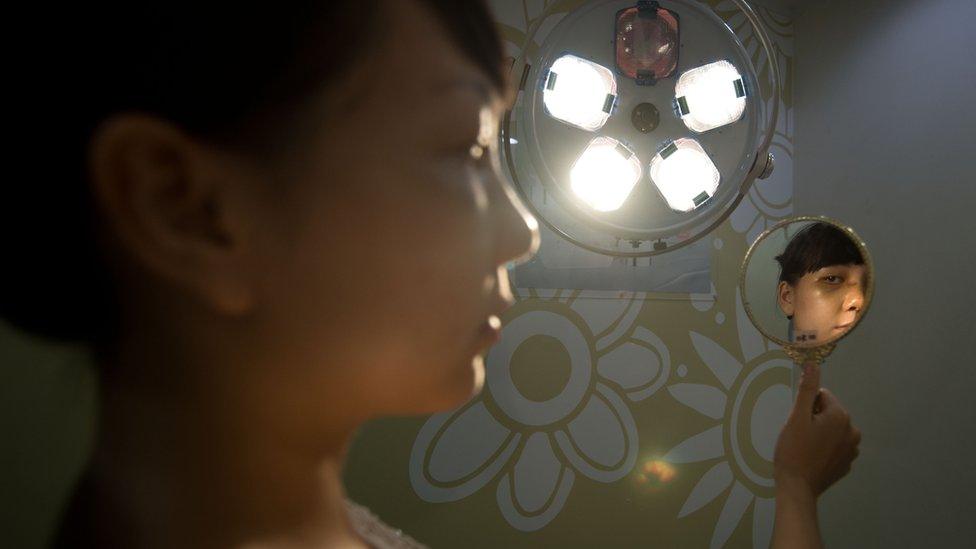 Girl holds mirror up to examine her face post-operation