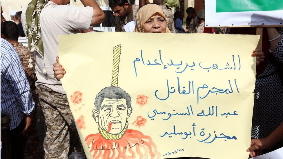 A Libyan woman holds a poster reading in Arabic: 'The people want the death penalty for Abdullah Senussi for the Abu Salim massacre' as they demonstrate outside a court against the ex-intelligence chief