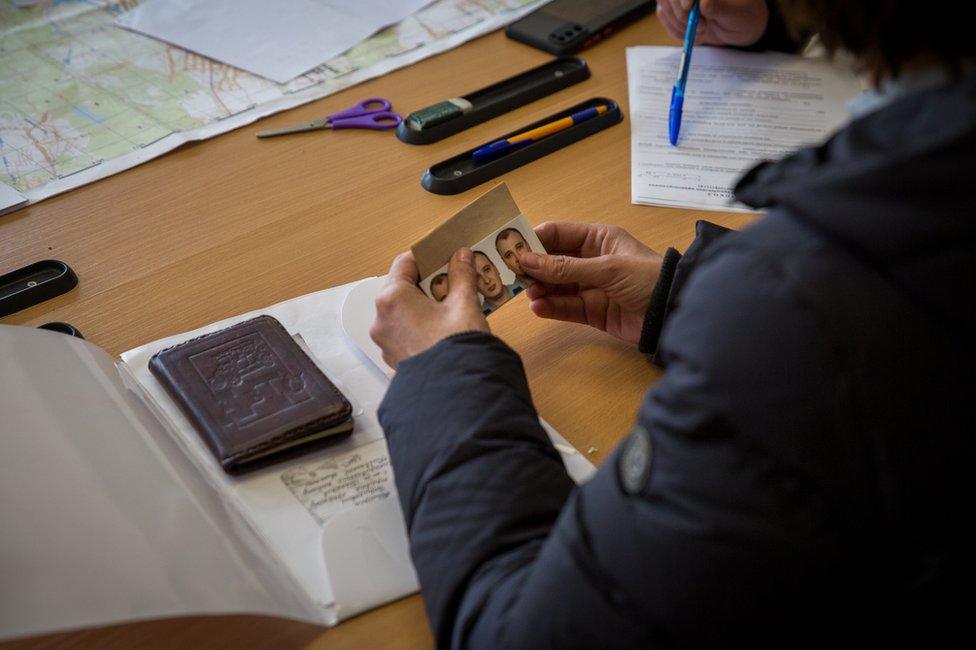 Olena Kuksa holds passport photographs of her missing husband at the police station.