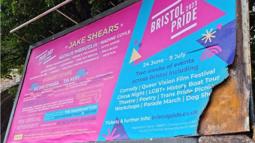 A bright pink and blue billboard with details of the Bristol Pride event on, that has been partially damaged by fire