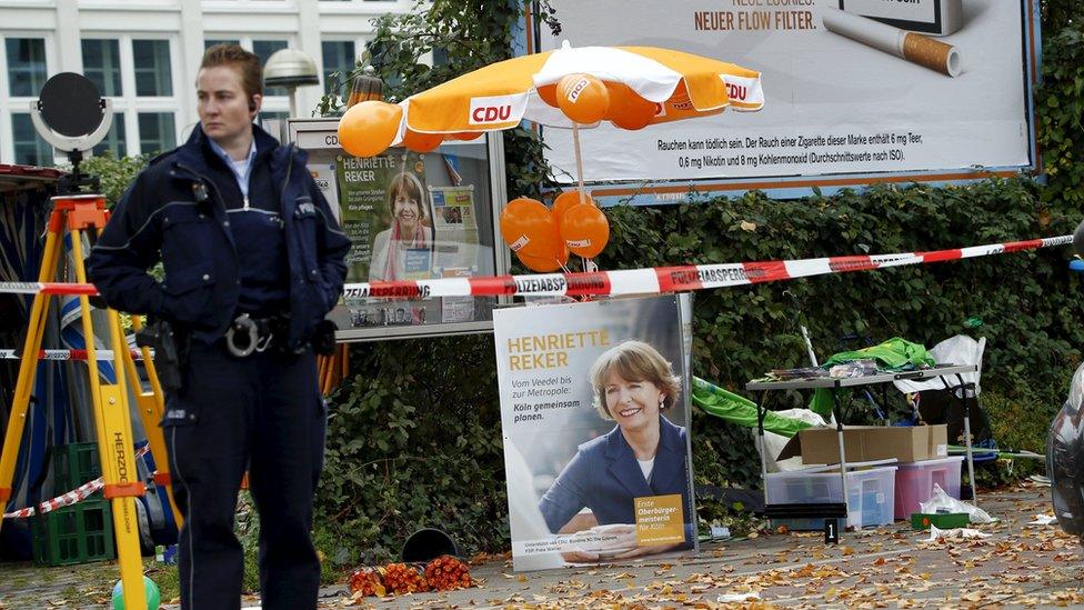 A police officer stands guard next to an election campaign poster of Henriette Reker in Cologne, Germany October 17, 2015.