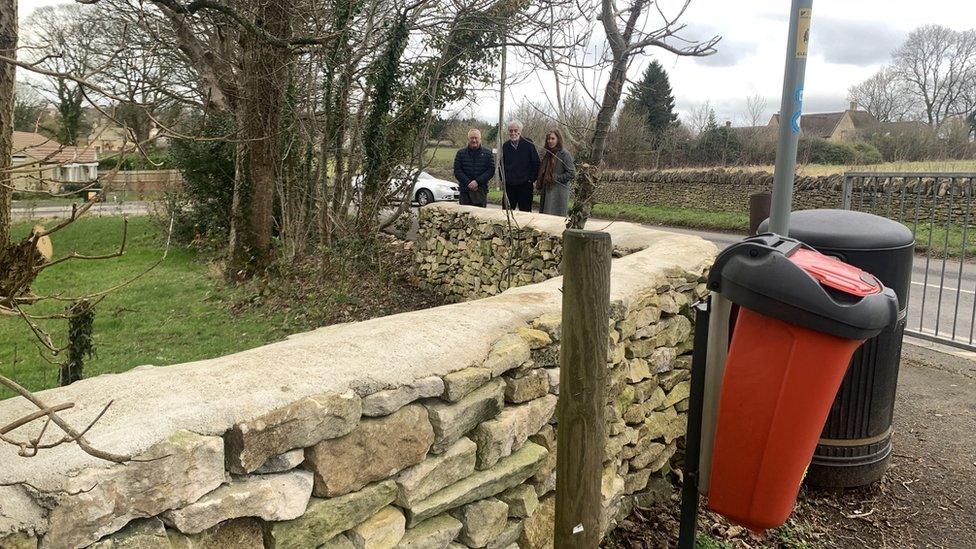 Two men and a woman looking at the rebuilt boundary wall