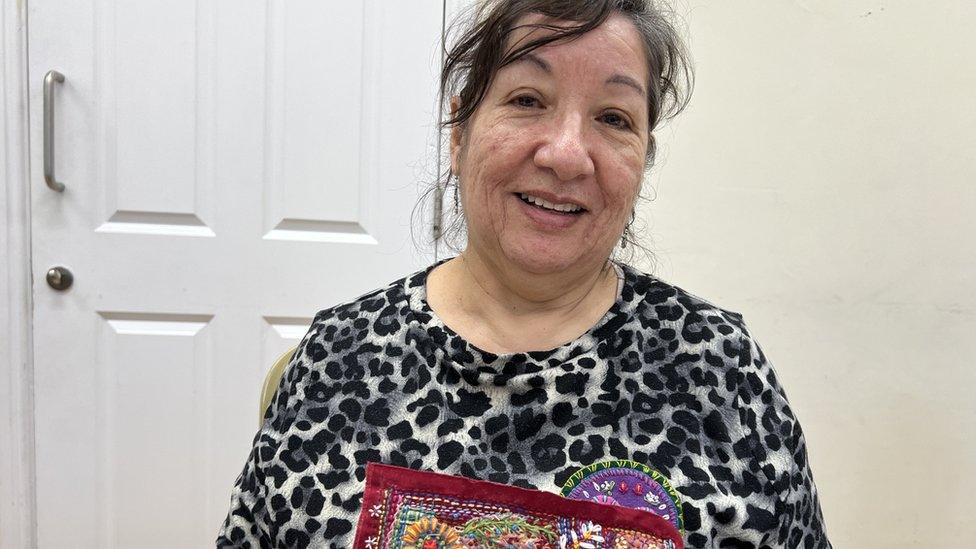 Jeanette looking at the camera, holding her stitching work