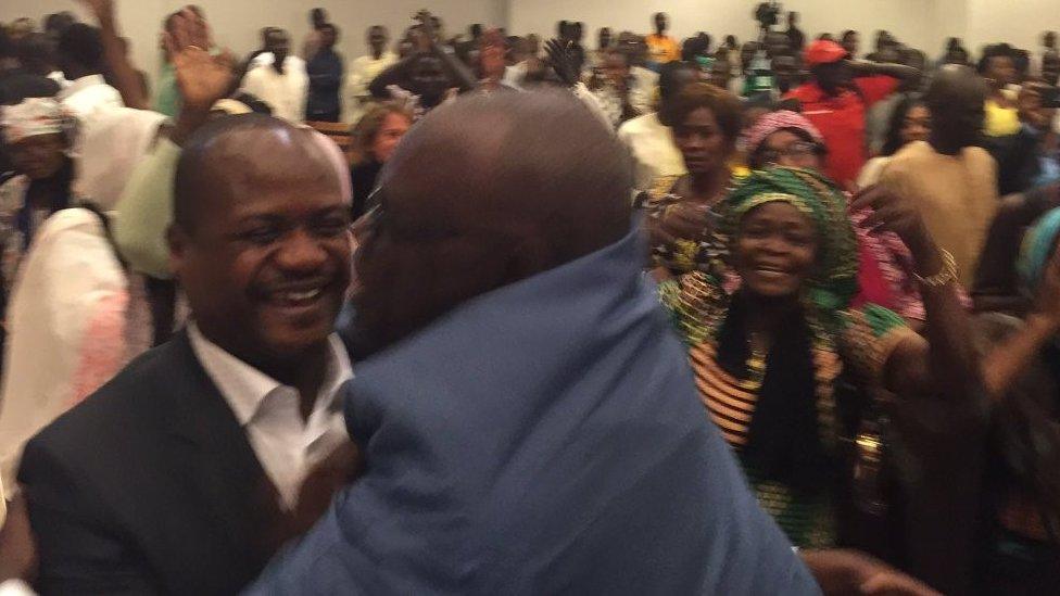 Two men hug each other while others cheer behind them in the courtroom