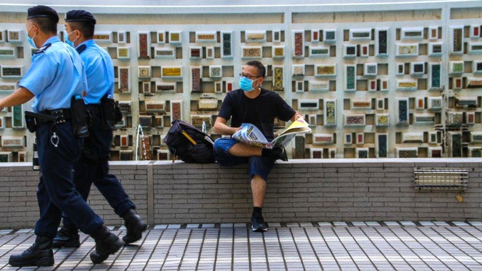 Police walk past a man sitting reading a newspaper