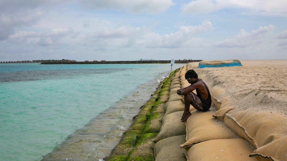 A man sits on sandbags beside water