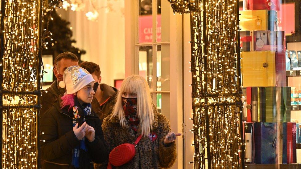 Shoppers wearing face coverings to combat the spread of Covid-19, leave through the decorations adorning a doorway of a store in central London on December 21, 2021