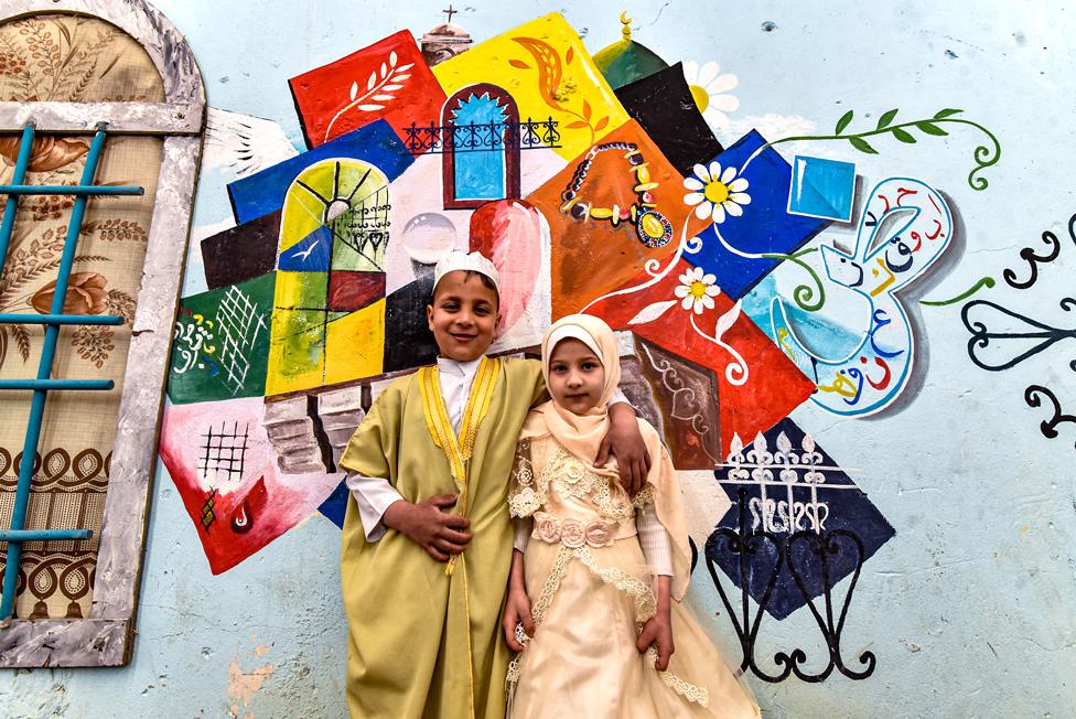 Children pose in front of street art depicting cultural elements including mosques, and old window lattices of the old town of Iraq's northern city of Mosul