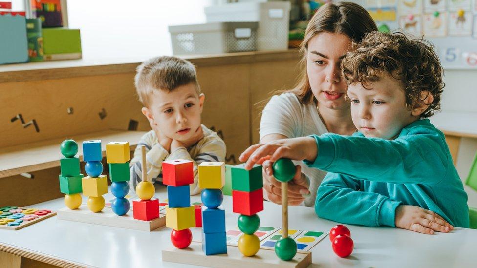 Two young children playing with toy blocks with an adult woman