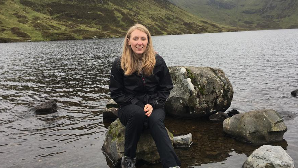 A woman siting on a rock by a river smiles at the camera