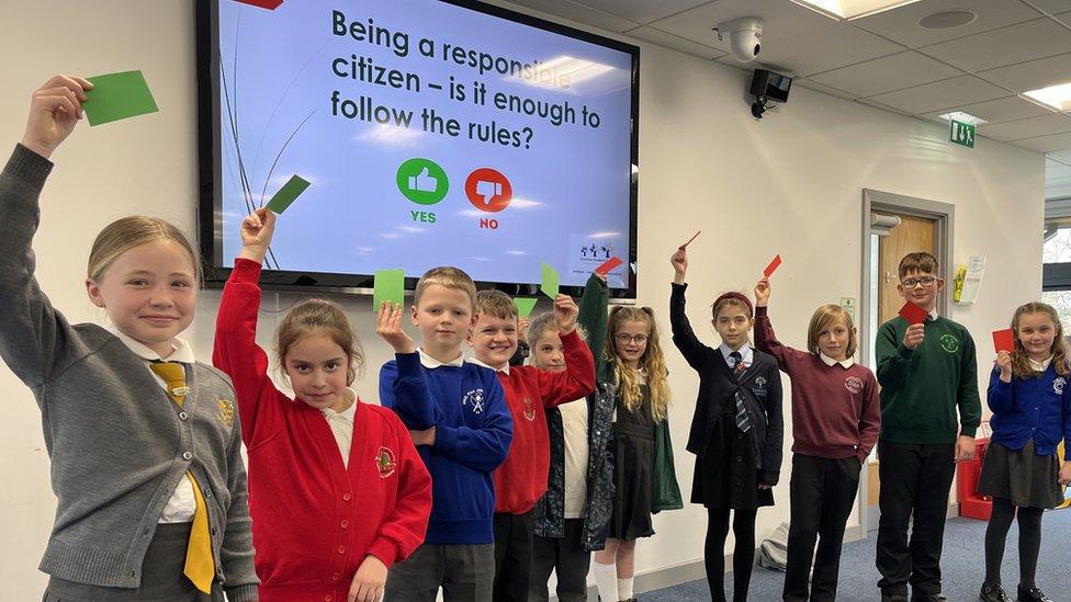 Ten young people in different school uniforms stand in a line with green and red cards held up