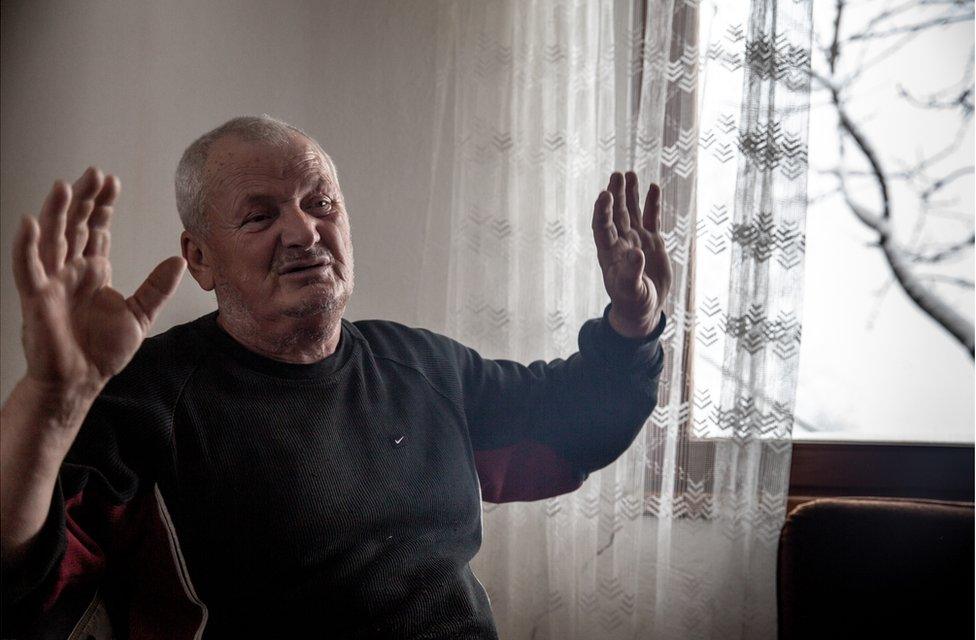 A man sits next to a window and holds up his hands