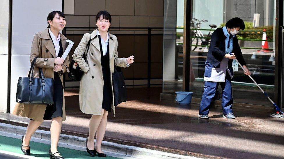 Women walk past a cleaner in Tokyo's Ginza district on April 3, 2019