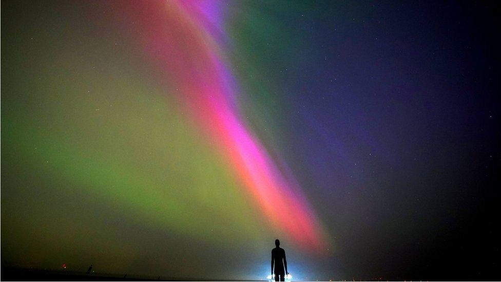 The aurora borealis, also known as the northern lights, glow on the horizon at Another Place by Anthony Gormley, Crosby Beach, Liverpool , Merseyside