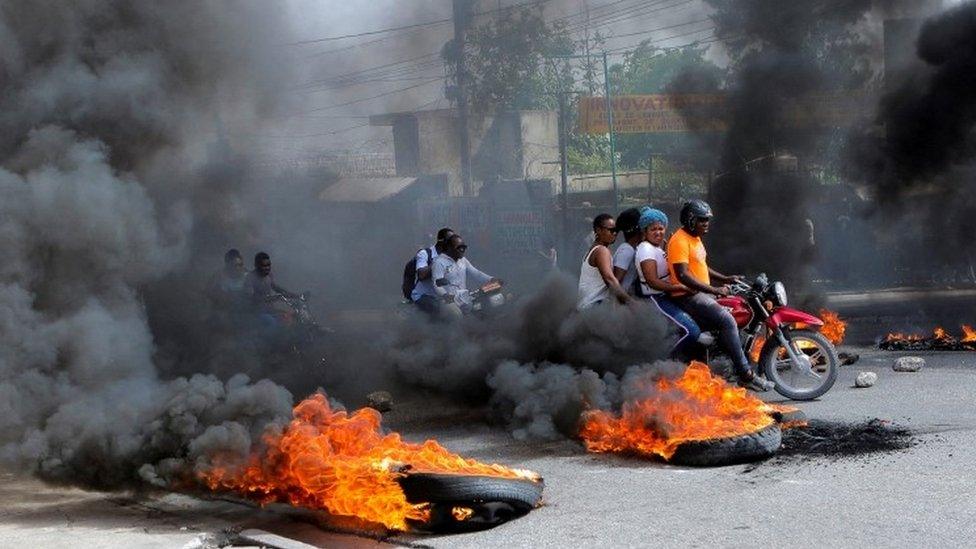 Motorcycle drivers pass through a burning road block as anger mounted over fuel shortages that have intensified as a result of gang violence