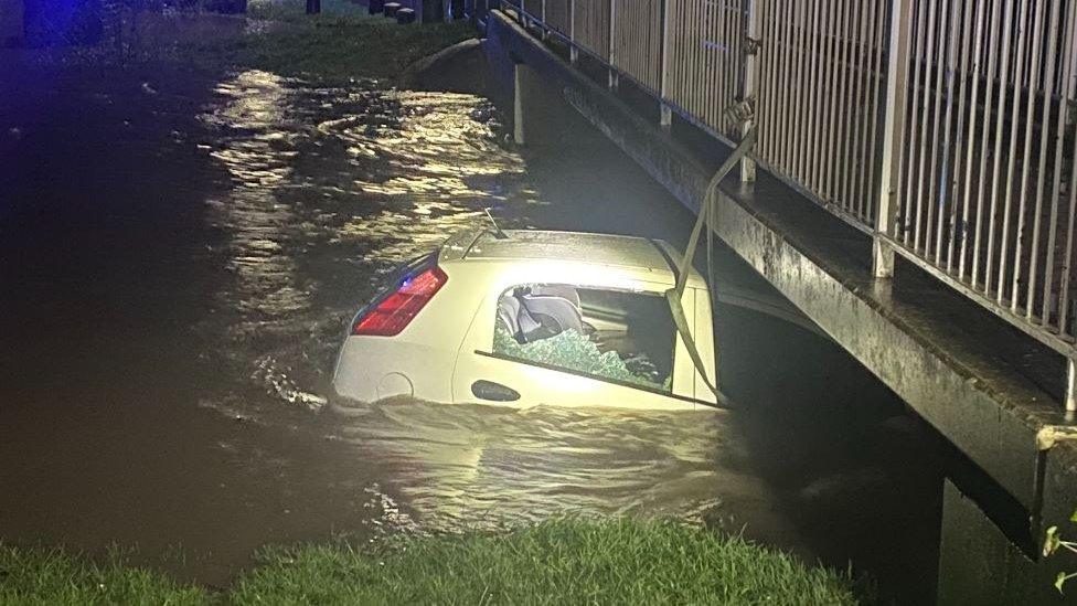 Car seen with smashed window, tethered to a bridge