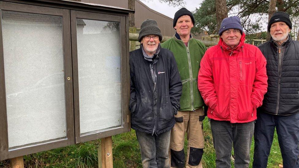 Four men stand by notice board