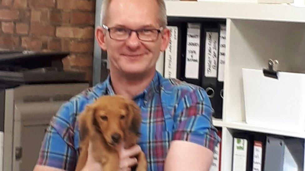 Tomasz holds Ralphy the dog on his lap in the office