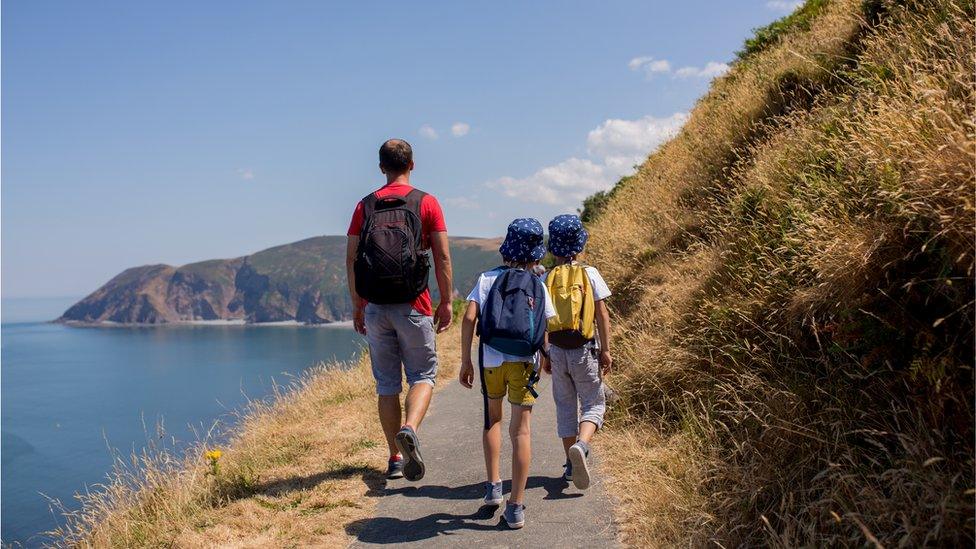 A father and two boys walk along the Devon coastline