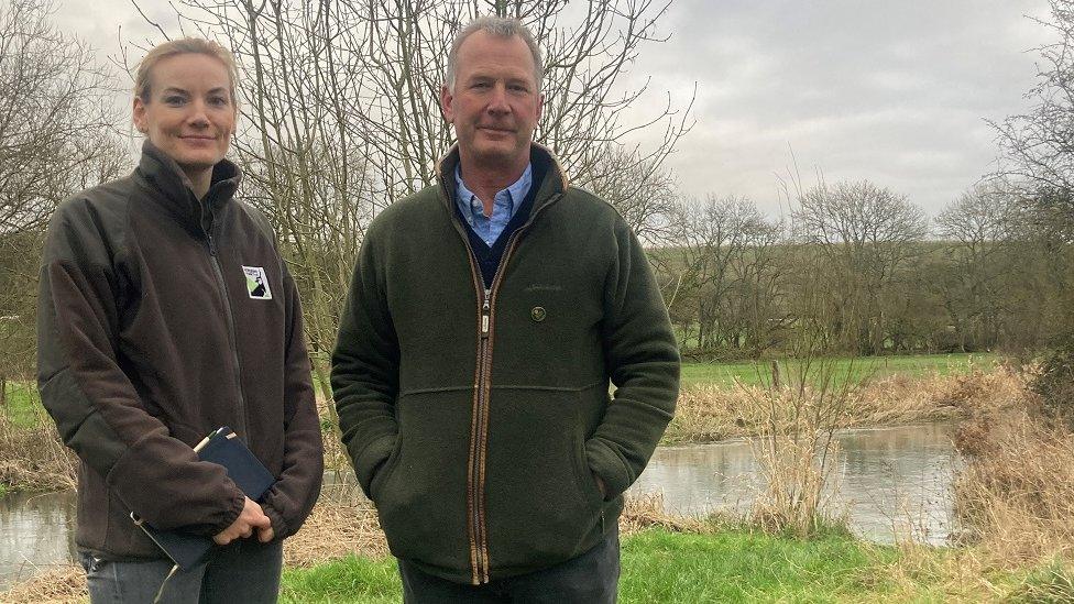 Alice Eley from the Wiltshire Wildlife Trust and farmer Josh Stratton look at the camera while standing in front of the river