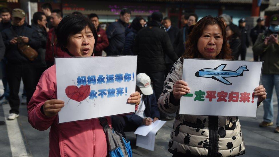 Two relatives of passengers missing on Malaysia Airlines MH370, reads hold placards during a gathering of relatives outside the Lama Temple in Beijing on March 8, 2016.