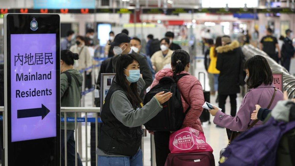 A woman stands next to a sign that says 'mainland residents' and directs passengers