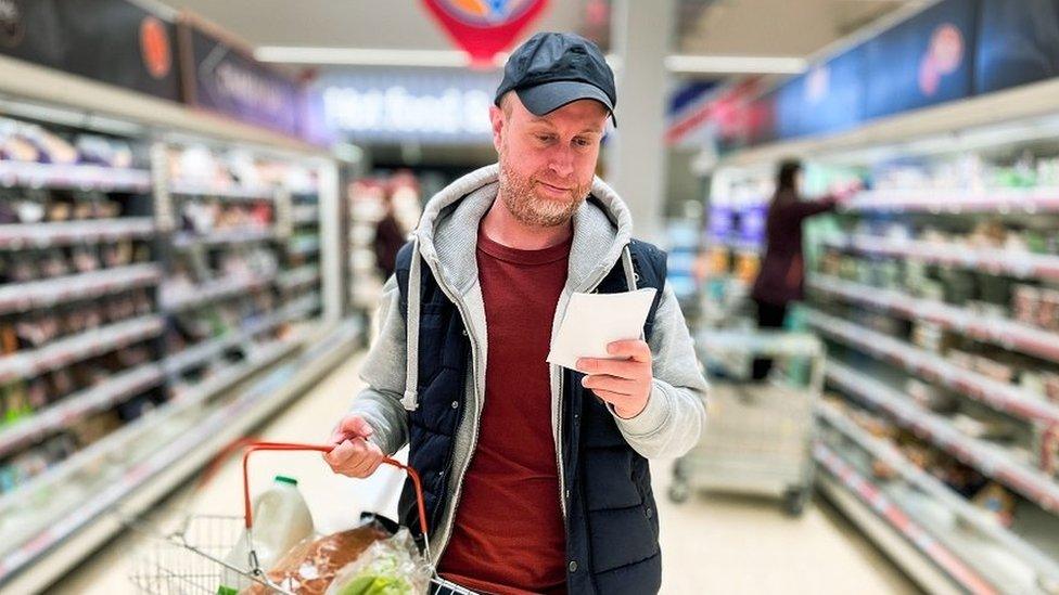 Man looks a shopping list as he walks through a supermarket aisle