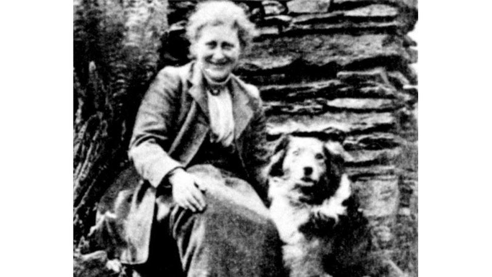 A black and white photo of Beatrix Potter, sitting down with her dog.