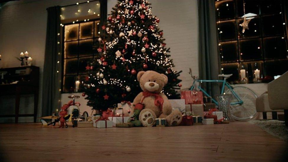 A Teddy bear and presents in front of a Christmas tree