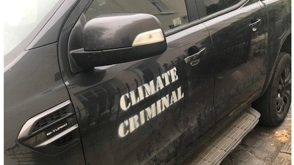 A black truck with "climate criminal" stencilled in white along the side