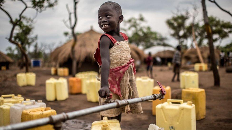 A girl smiles as she fills up her jerrycans with water