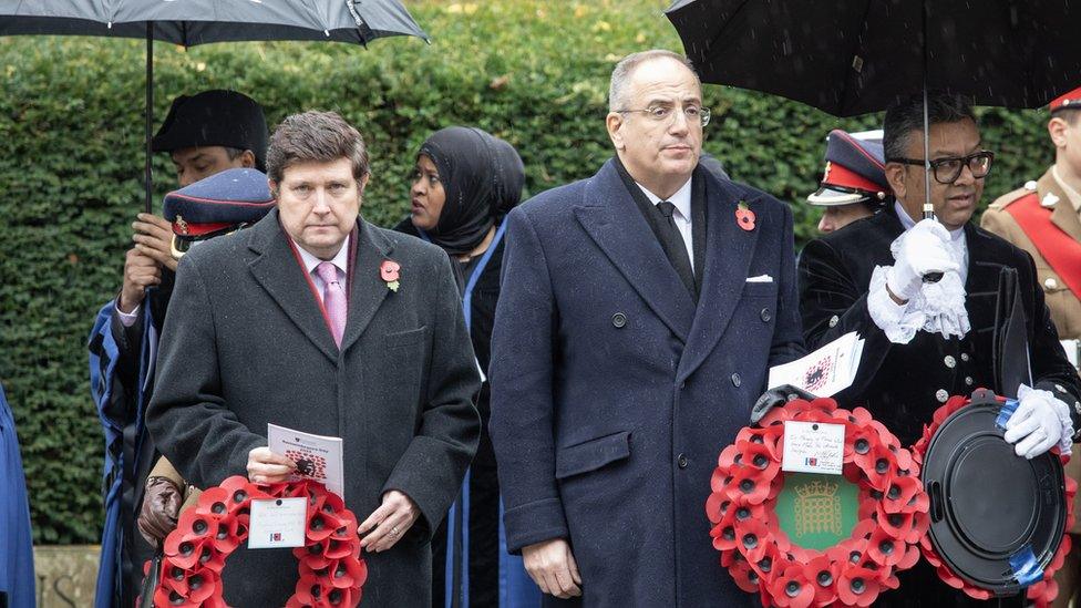 Men in long black coats carry poppy wreaths