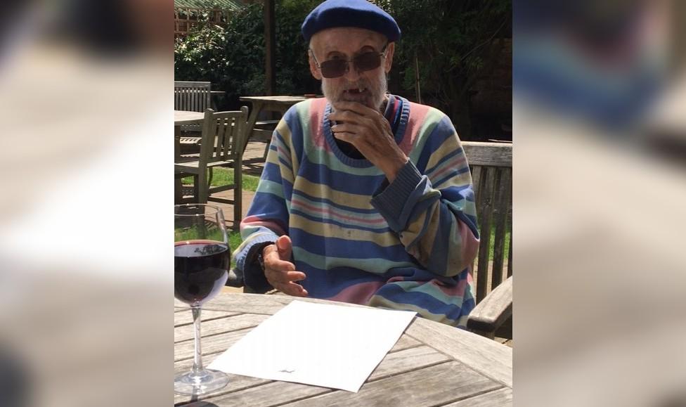 David Kirke in a colourful striped jumper with a glass of red wine, holding his hand to his chin