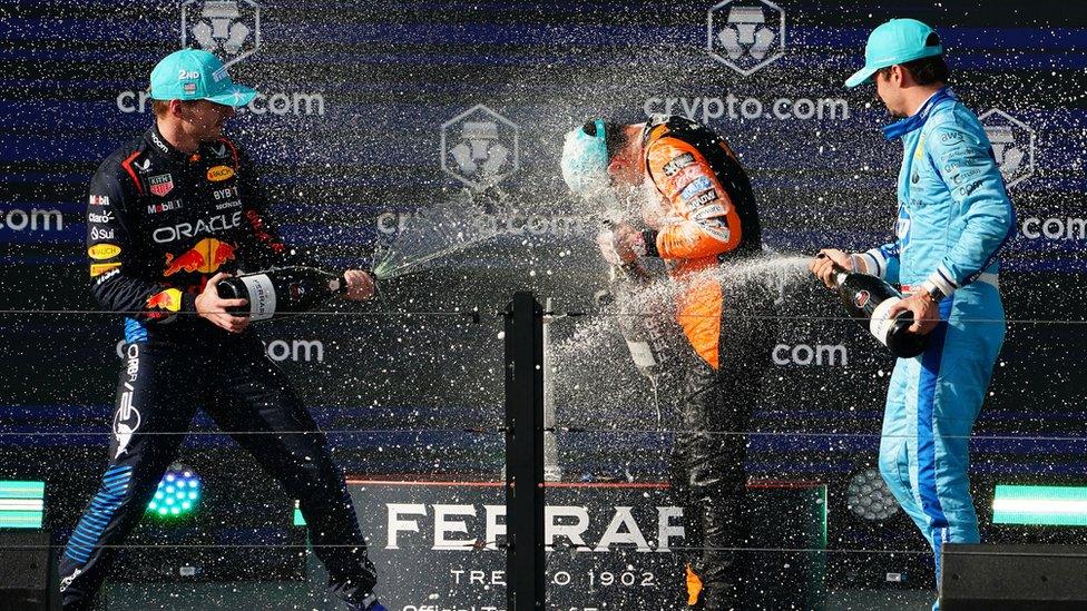 Drivers spray each other from bottles on a podium