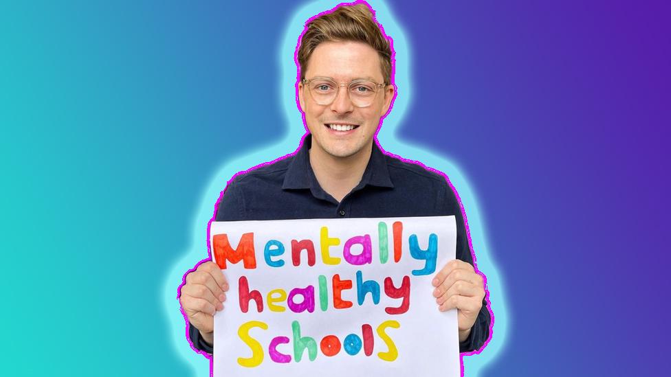 Dr Alex holds sign saying 'mentally healthy schools'