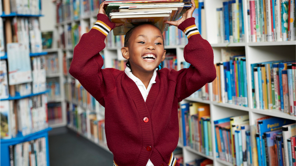 A young girl holds books over her head with a huge smile across her face