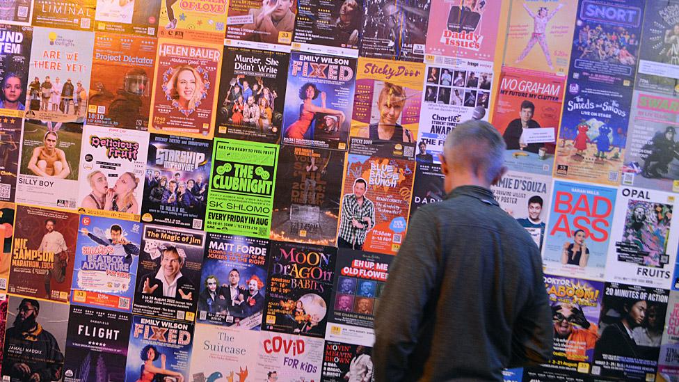 A man standing in front of a wall of posters for shows at the Edinburgh Fringe