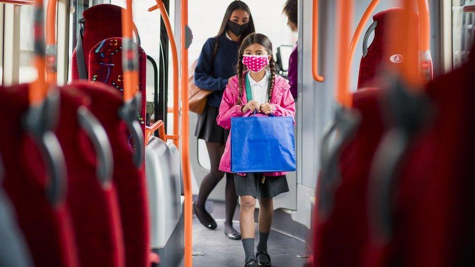 Two girls getting on a bus wearing face coverings