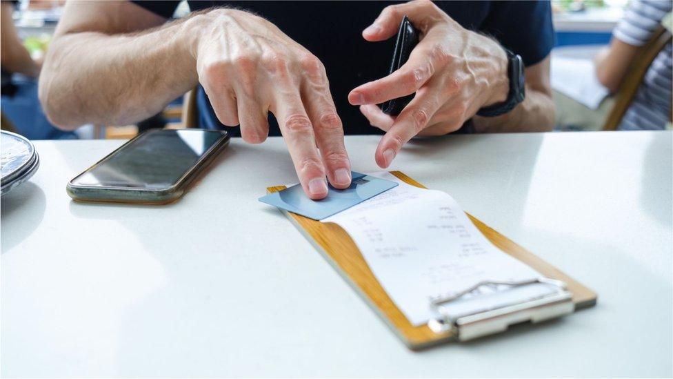 A man's hand puts a credit card on a restaurant bill