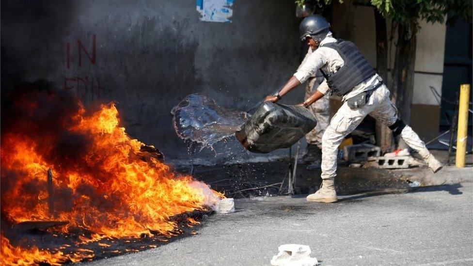 A police officer puts out a burning fire as demonstrators take part in a protest against Haiti's President Jovenel Moïse, in Port-au-Prince, Haiti February 14, 2021.