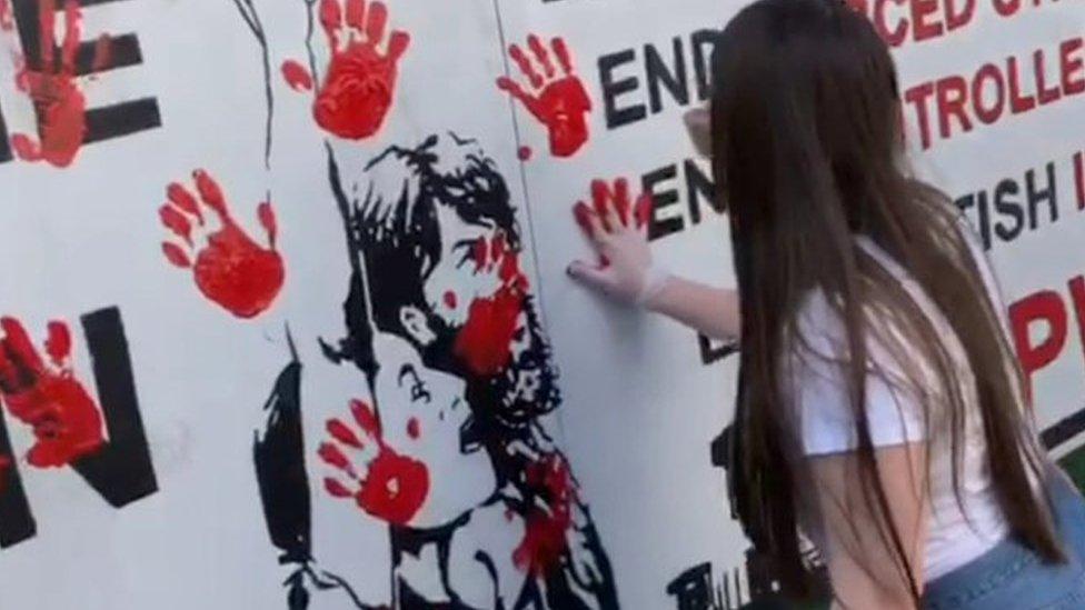 A woman smears a red hand print on a wall