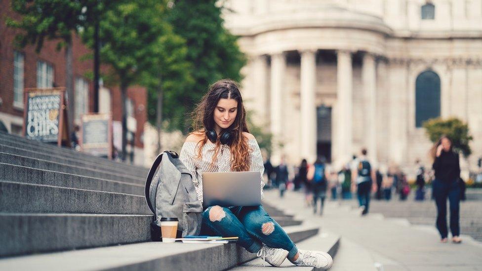 Happy girl sitting on some steps, working on her laptop