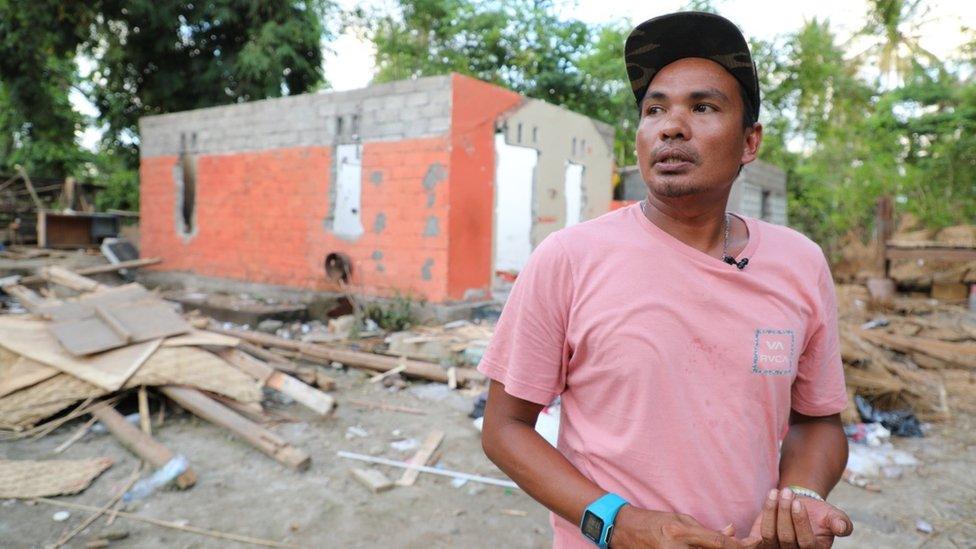 Damar in front of ruins that once his home