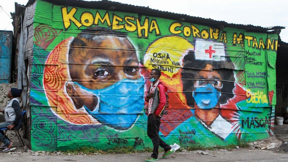 A man wearing a face mask walks past a mural depicting health workers by the Mathare Roots Society initiative group that uses the graffiti form of creative art to inform and sensitise the residents of Mathare slums.