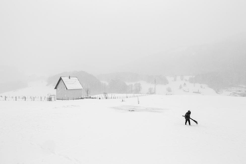 In the North of Montenegro a shepherd is walking to his herd of sheep with a self made broom in his hand. The broom was used to wipe off the snow lying on the back of the sheep.