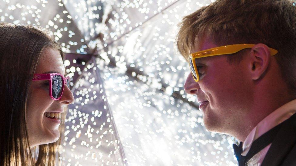 A woman and a man wearing sunglasses in front of a bright light feature