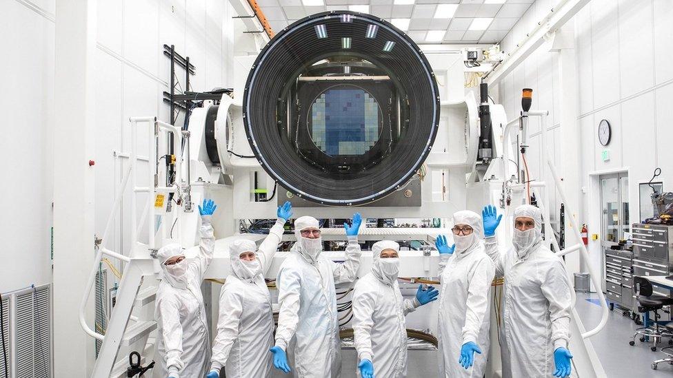 Scientists stand below a giant camera lens, which is the same size as a small car.