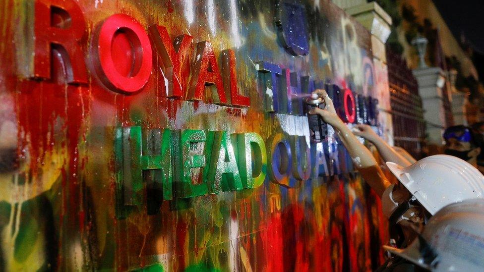 A person stands in front of the paint-covered plaque with lettering on it during a rally in Bangkok